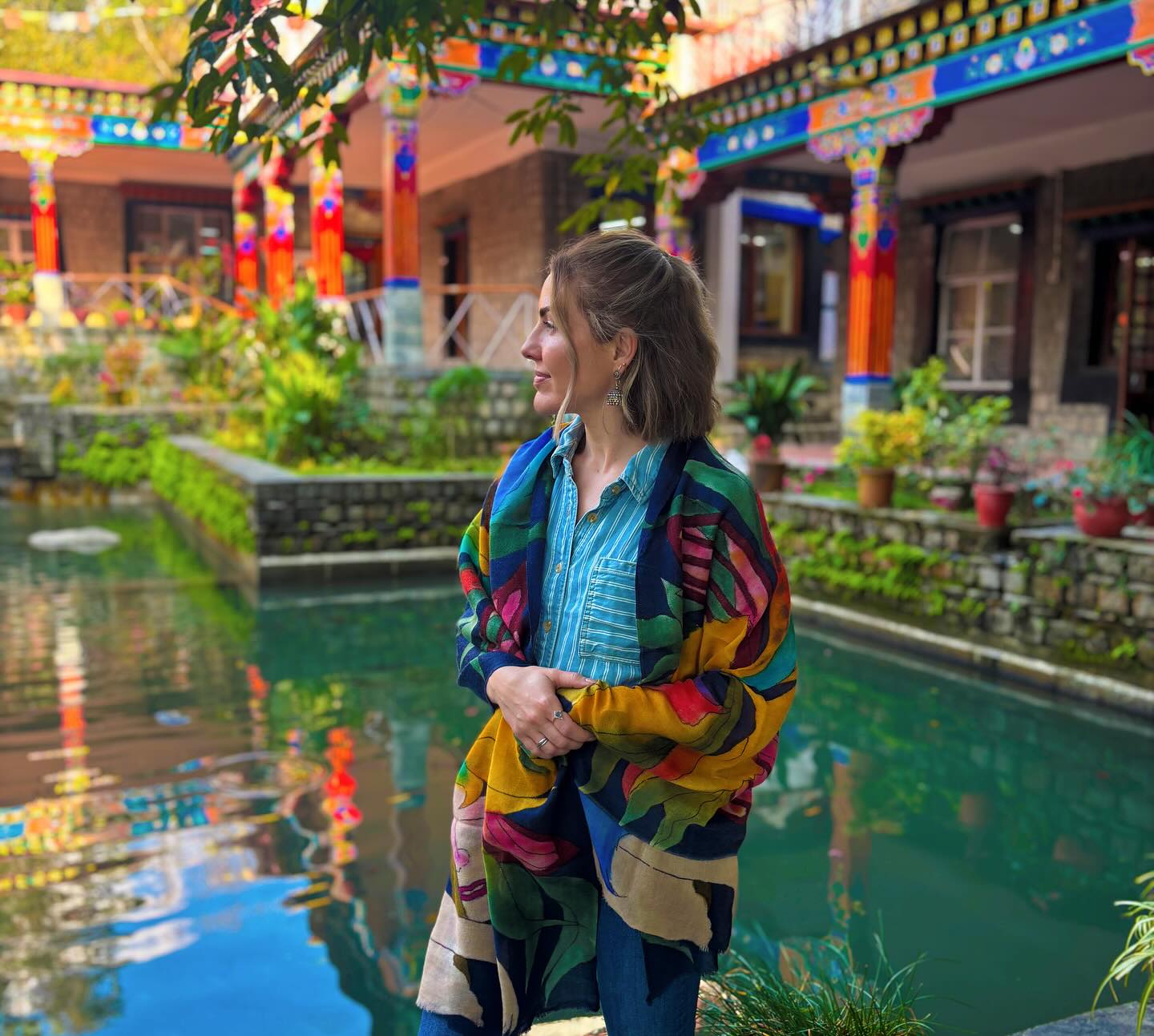 Kirsten standing by a courtyard pond framed by trees and colorful architecture in India